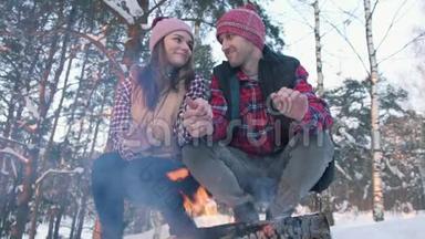 一对穿着红色衬衫的年轻人在树林里，温<strong>暖</strong>他们的手在火边，<strong>冬季</strong>野餐